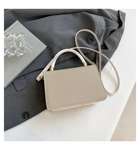 Detail of beige textured crossbody bag with white top handle and elegant gold hardware