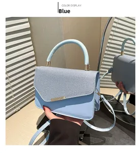 Detail of light blue crossbody bag with matte leather stitching and gold metal bar accent