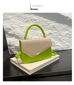 Detail view of a green leather and beige canvas handbag with gold hardware on white books
