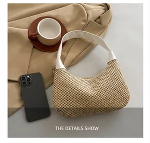Draufsicht einer Stroh-Halbmondtasche mit weißem Lederriemen auf einem beigen Blazer
