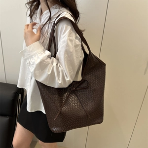 Dark brown woven leather tote bag with bow detail on a shoulder strap for daily commuting