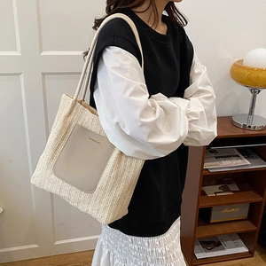 Large straw tote bag with leather pocket shown on shoulder in cozy indoor setting