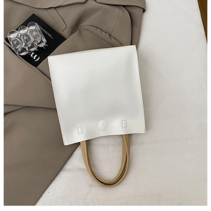 Close-up of a white leather tote bag with khaki handles and circular stitch detailing