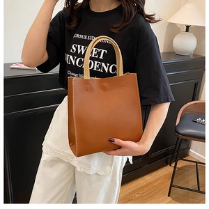 Brown tote bag with cream handles shown in a modern home setting by a model