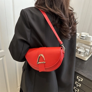 Fashionable red leather saddle bag with gold metal stirrup buckle worn as a shoulder bag
