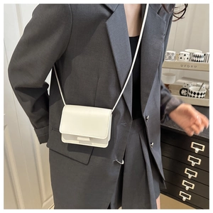 White minimalist mini flap crossbody bag shown on a model with a thin shoulder strap