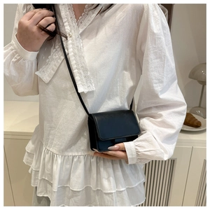 Detailed view of a black minimalist small square crossbody bag worn by a female model