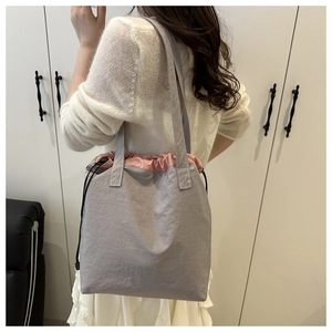 Detail of grey tote bag with pink drawstring closure and wide shoulder strap on model