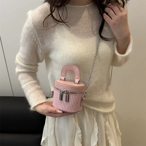 Mini pink cylinder bag with woven detail and chain strap shown in a lifestyle indoor setting