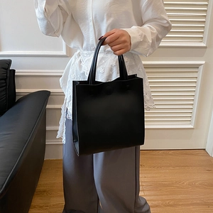 Minimalist black rectangular leather handbag with cylindrical handles for modern women