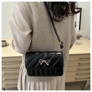 Detail view of a black quilted crossbody bag with a golden bow and a thin shoulder strap