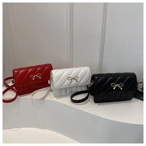 Détail de trois sacs bandoulière matelassés rouge, blanc et noir avec nœuds dorés