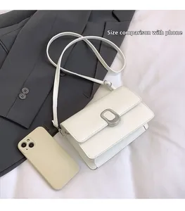White leather crossbody bag size comparison with a smartphone on casual suiting