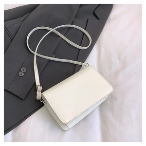 Detailed view of a white minimalist crossbody bag on a grey blazer over fabric
