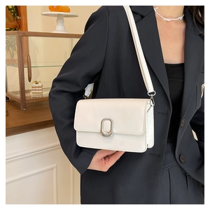 Detail of a minimalist cream square bag with silver oval metal buckle on a shoulder strap