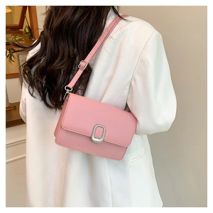 Detailed view of pink leather crossbody bag with silver oval metal clasp on a white suit model
