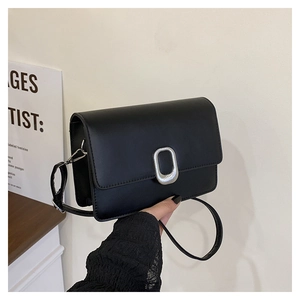 Detail of black leather crossbody bag featuring a large silver oval metal buckle
