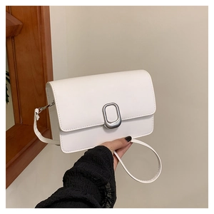 Close-up of white minimalist flap bag featuring an oval silver textured metal buckle