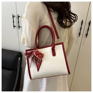 Detail of white snakeskin tote bag with red leather trim and decorative heart scarf