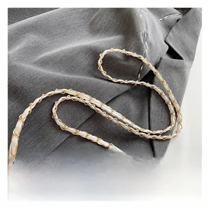 Detailed close-up of white leather interwoven with a gold metal chain strap on a blazer