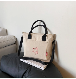 Detailed view of canvas bucket bag with cartoon bear print and black strap on a book