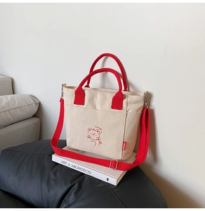 Detail of canvas bucket bag with red contrast straps and cartoon bear print on white books