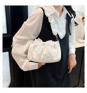 Détail du sac en satin blanc avec un grand nœud et une bandoulière à volants et crochets