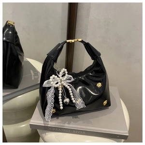 Detalle de bolso en charol negro con herrajes de garra dorada y colgante de lazo de perlas