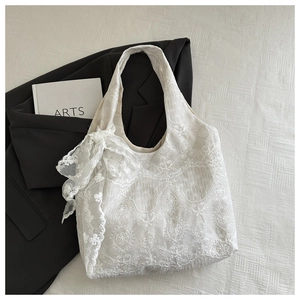 Detail of white lace tote bag featuring intricate floral patterns and a large side bow
