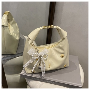 Détail du sac crème avec boucle dorée et pendentif noeud en dentelle de perles