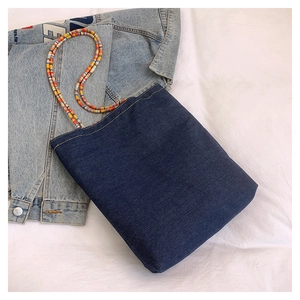 Dettaglio borsa tote in denim blu con tracolla di perline colorate su tela bianca