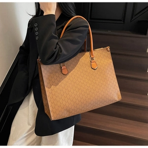 Close-up of brown large tote bag with M-pattern texture on wooden stairs background