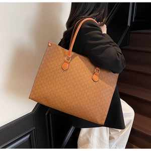 Close-up of brown tote bag with M-pattern print and rivets worn by a model