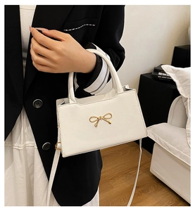 Gros plan du nœud doré sur un sac à bandoulière blanc minimaliste en cuir