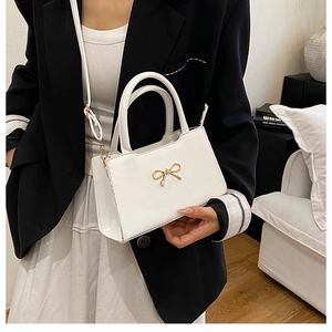 Détail d'un mini sac blanc avec nœud doré métallique et texture en cuir lisse élégante