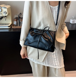 Detail of minimalist black bow crossbody bag with ruched texture and elegant flap design