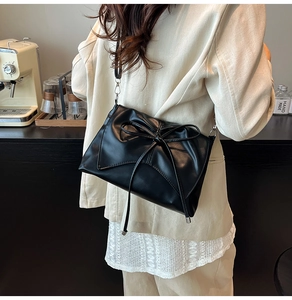 Détail d'un sac à bandoulière en cuir noir avec un grand nœud et des crochets argentés