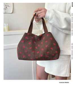 Detail of strawberry print on brown corduroy tote bag held by a model in a modern room