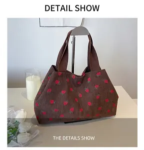 Detail view of brown corduroy tote bag featuring red strawberry print on a metal stand