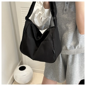 Minimalist black canvas hobo bag with wide shoulder strap shown on a female model