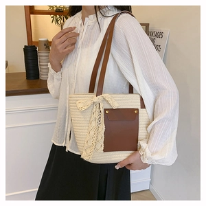 Detail of woven straw tote bag with brown leather pocket and lace bow decoration