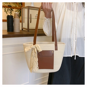 Detail of woven straw tote bag with brown leather pocket and delicate lace bow