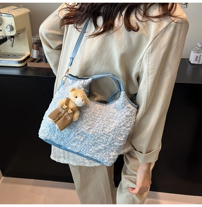 Détail du sac seau bleu clair texturé avec charme d'ours et poignées tissées chic