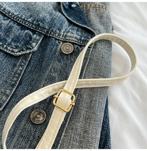 Détail du tissu en denim bleu avec boutons vintage et fine ceinture en cuir blanc