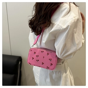 Detail view of pink cherry print crossbody bag with glossy finish on a female model
