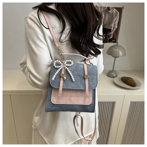 Détail du sac à dos bleu avec rabat en cuir rose et pendentif nœud en perles raffiné