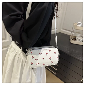 Detail of white square crossbody bag with cherry prints and double zipper closure