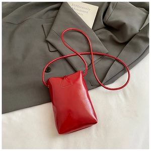 Détail du mini sac à bandoulière en cuir verni rouge vif sur un blazer gris chic