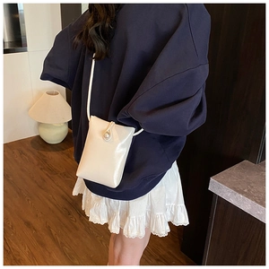 Détail d'un mini sac bandoulière blanc crème avec fermoir perle porté par un mannequin