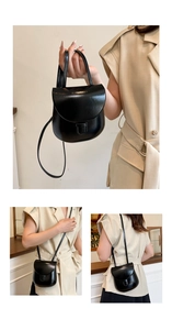 Detail of a minimalist black polished saddle bag with adjustable strap and top handle